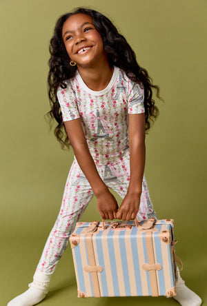 A Girl Wearing Fleur De La Tour Short Sleeve Stretch Jersey Kids Pj Set in a front view pose while holding a pastel suitcase
