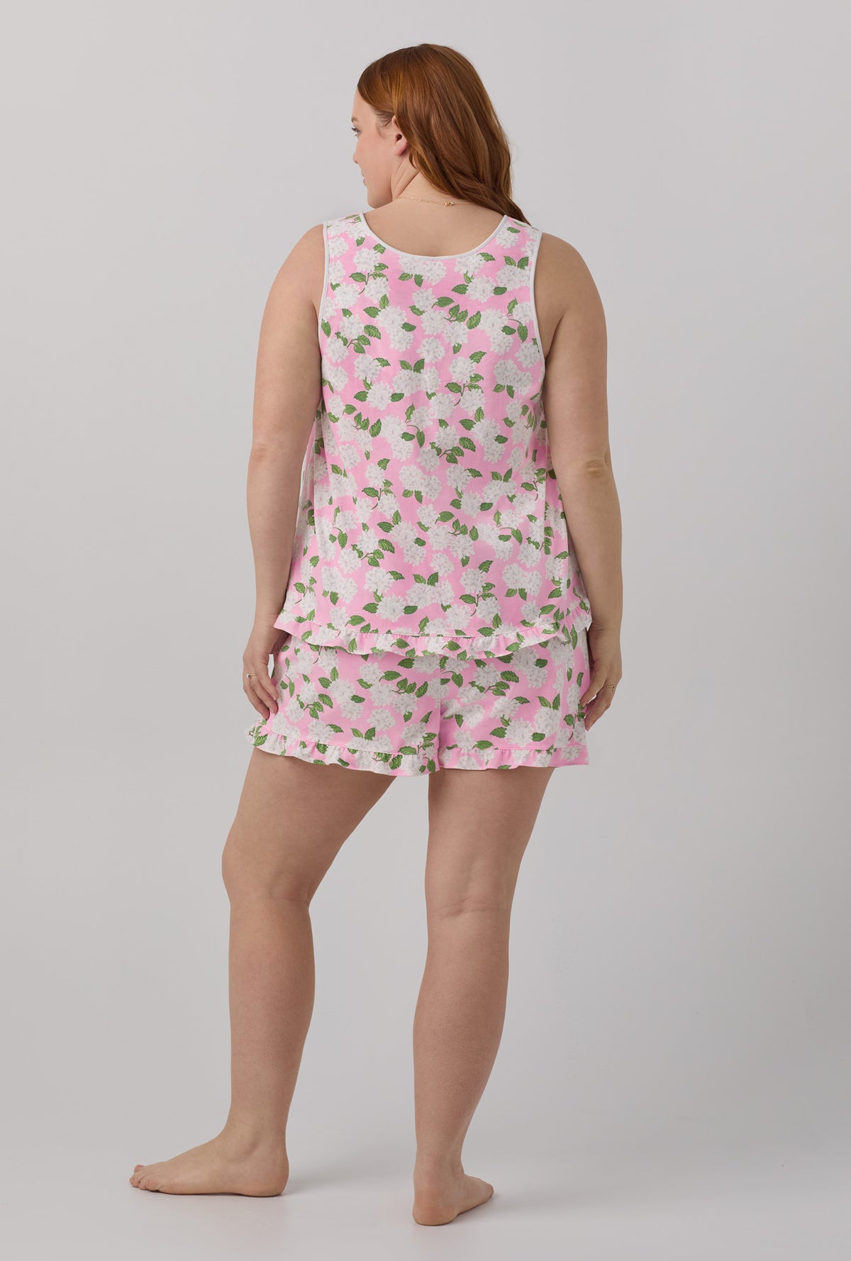 A lady wearing plus size pink Ruffle Tank Shorty Stretch Jersey plus size PJ Set with Pink Summer Hydrangea print.