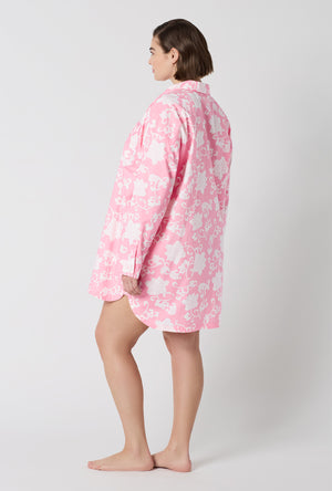 A Lady Wearing Plus Size Dynasty Pink High Low Woven Cotton Poplin Boyfriend Shirt in a side standing pose