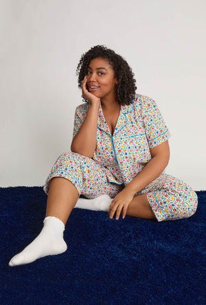 Woman wearing a plus size colorful pajama set sitting on a blue couch against a white background