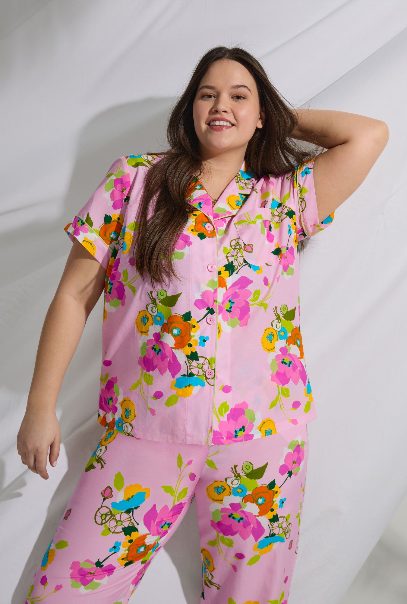 A lady wearing pink short sleeve classic woven cotton silk cropped plus size pj set with trina turk summer blooms print.