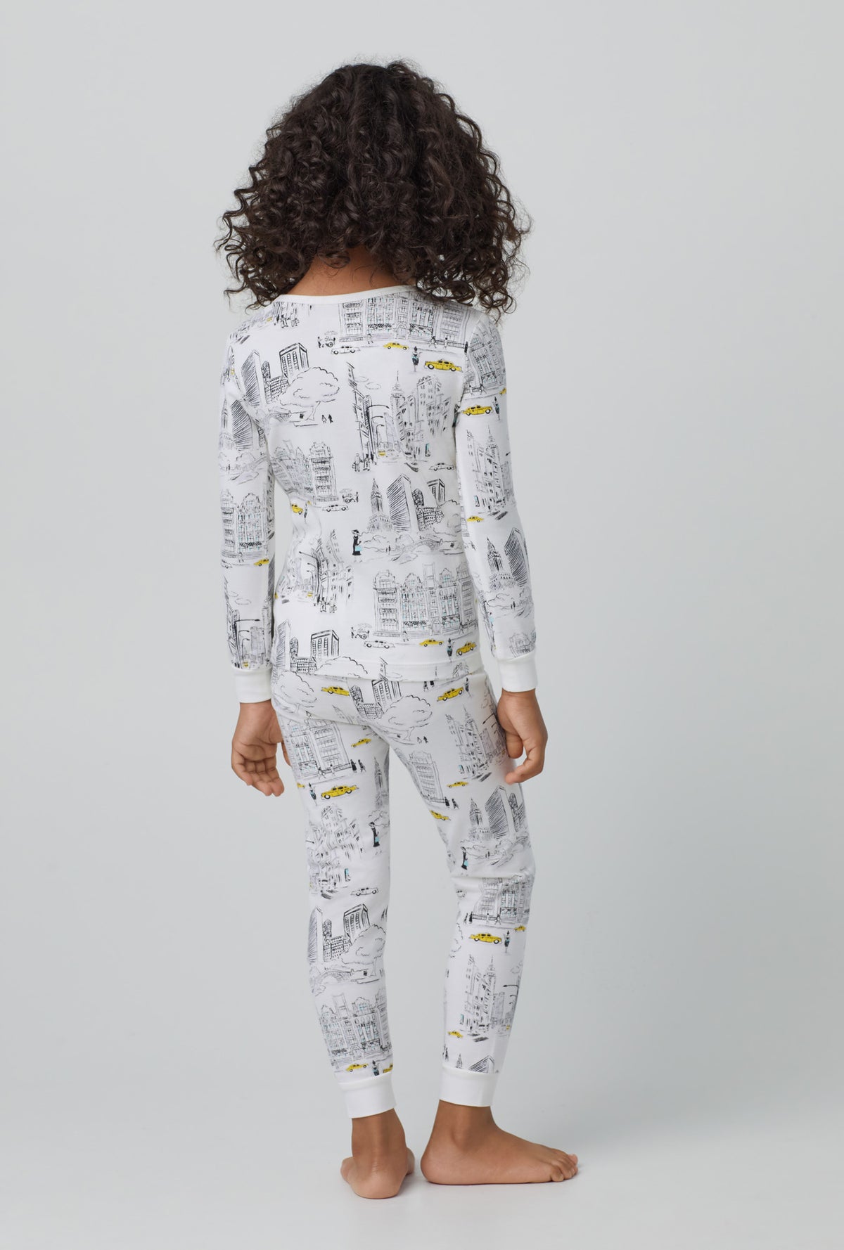 A kid wearing whiite long sleeve stretch jersey kids pj set with city that never sleeps print.