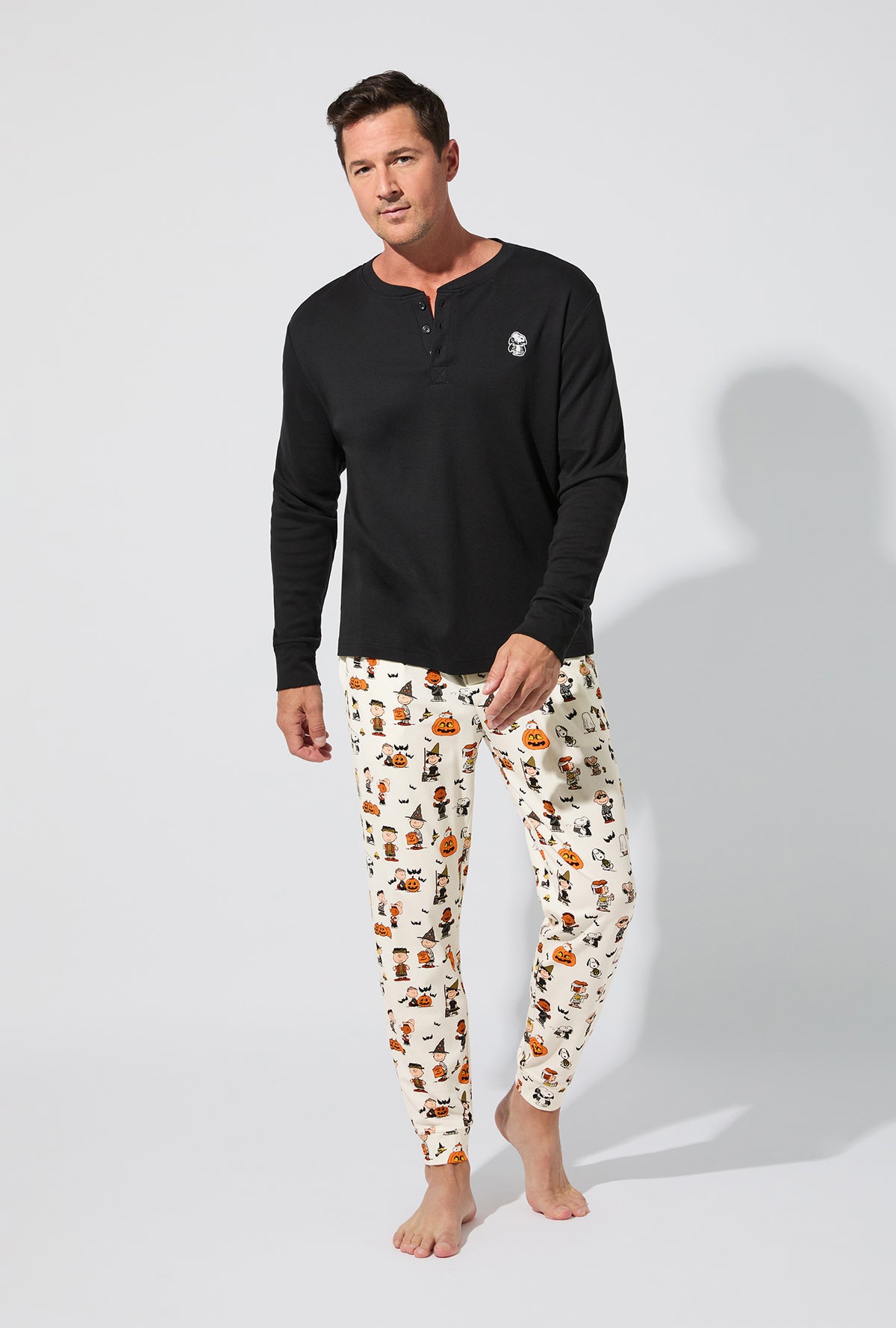 A man wearing Peanuts® Snoopy&#39;s Halloween Men&#39;s Long Sleeve Henley and Jogger Stretch Jersey PJ Set