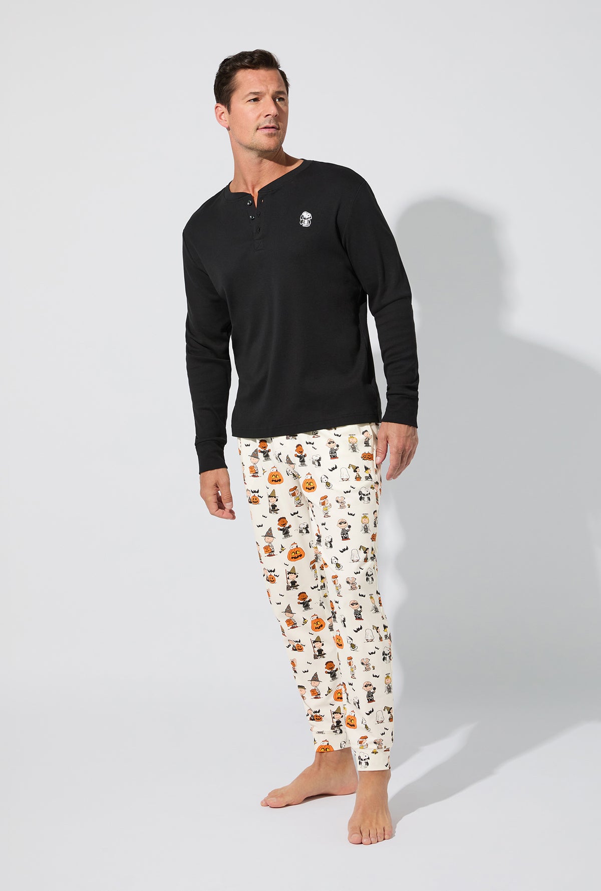 A man wearing Peanuts® Snoopy&#39;s Halloween Men&#39;s Long Sleeve Henley and Jogger Stretch Jersey PJ Set