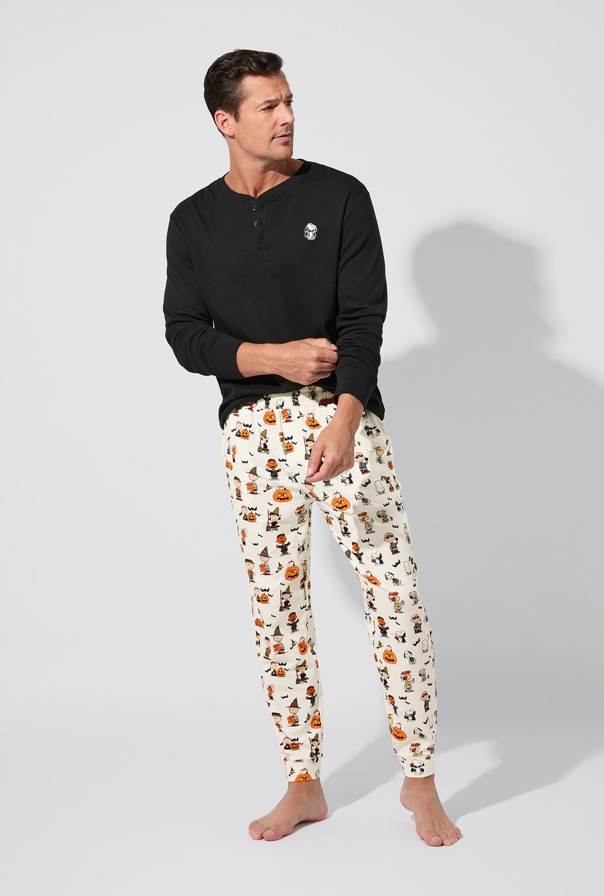 A man wearing Peanuts® Snoopy&#39;s Halloween Men&#39;s Long Sleeve Henley and Jogger Stretch Jersey PJ Set