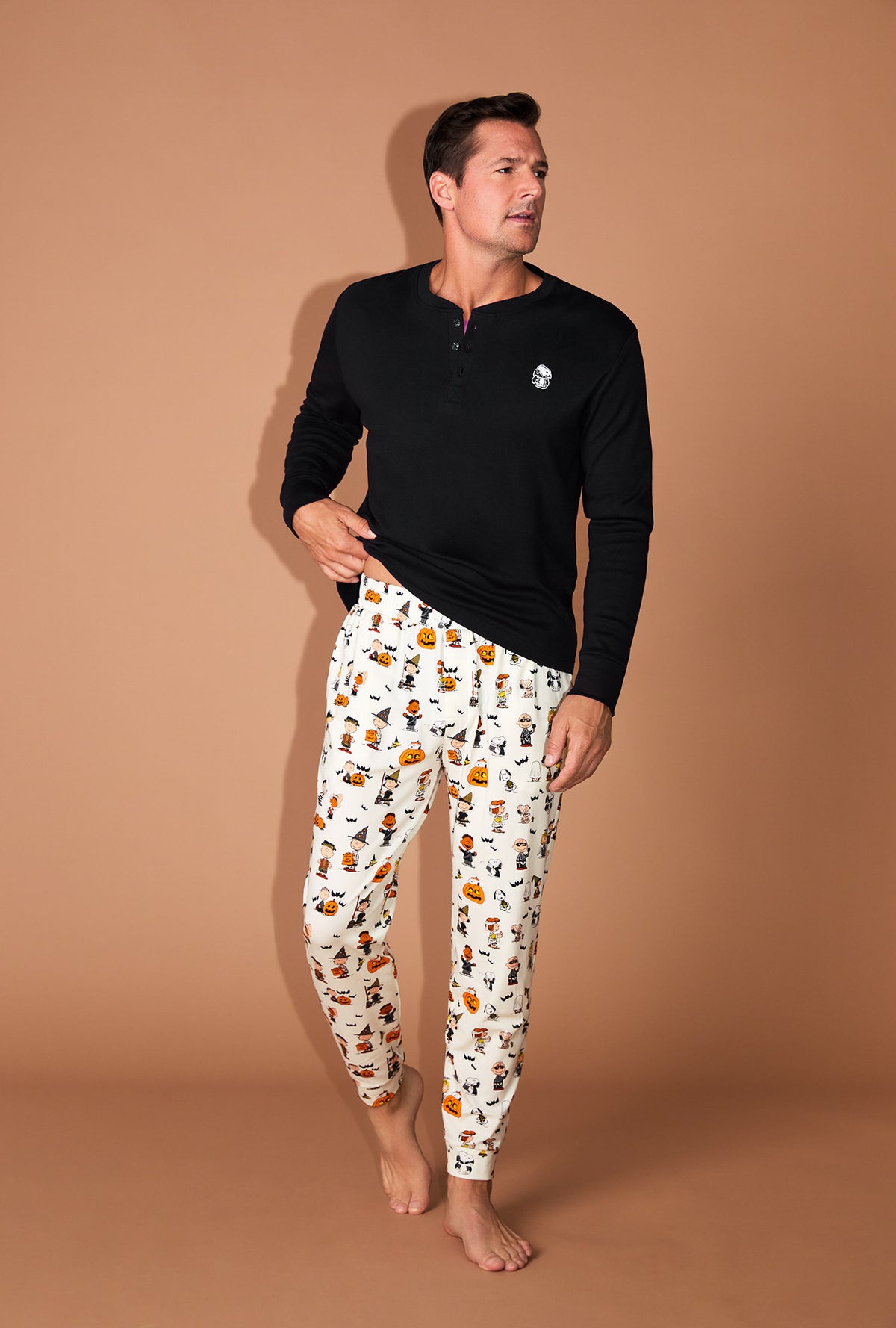 A man wearing Peanuts® Snoopy&#39;s Halloween Men&#39;s Long Sleeve Henley and Jogger Stretch Jersey PJ Set