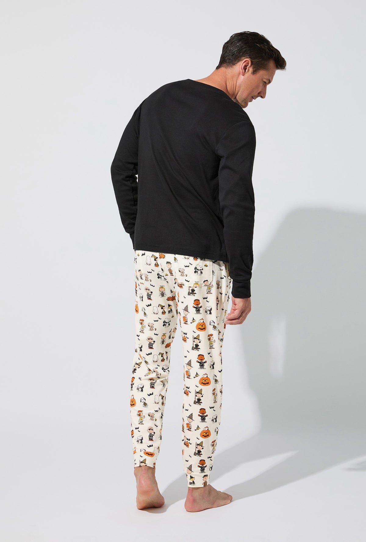 A man wearing Peanuts® Snoopy&#39;s Halloween Men&#39;s Long Sleeve Henley and Jogger Stretch Jersey PJ Set