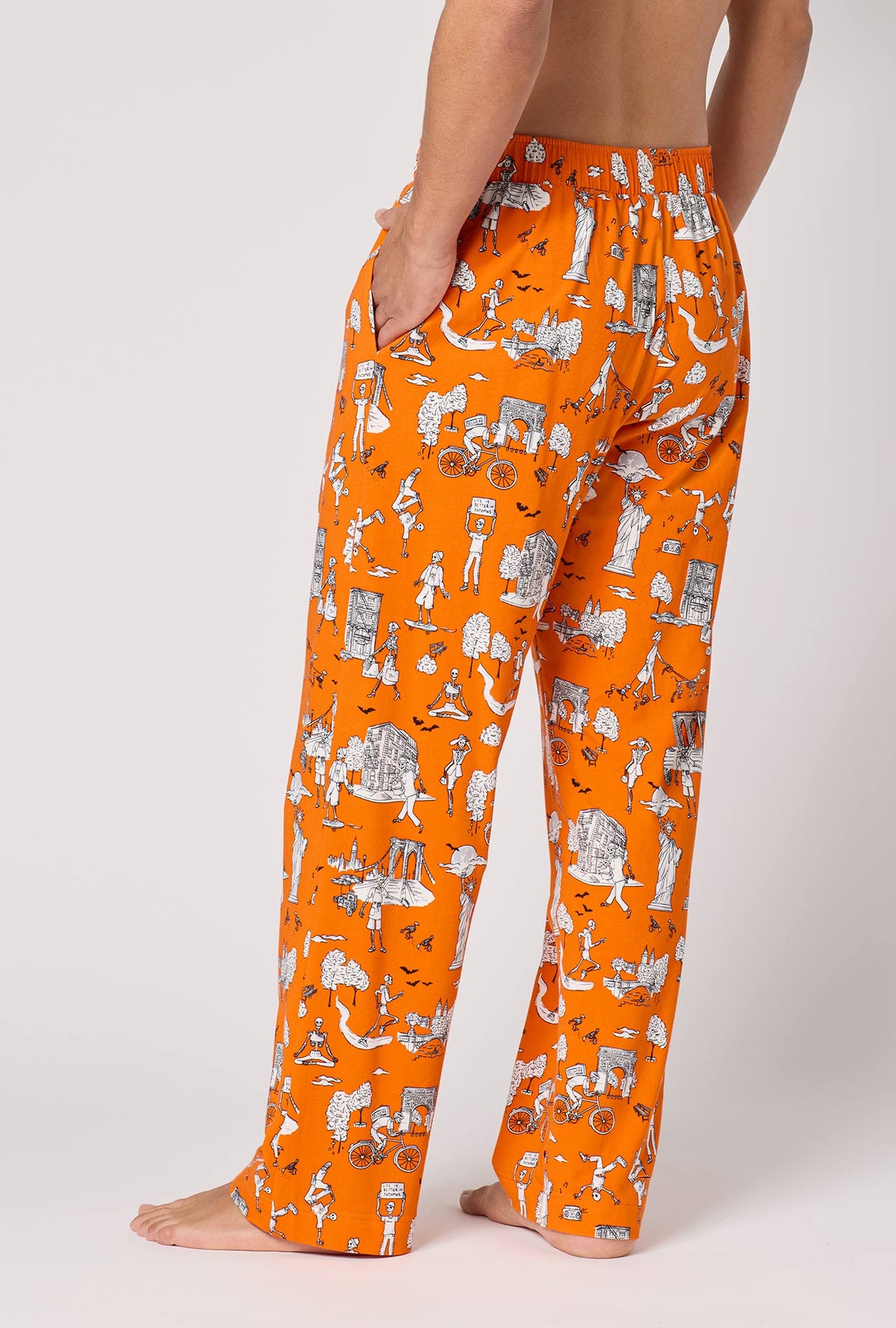 A Man Wearing Orange Spooky In The City Men's Stretch Jersey Pj Pant in a back view pose with one hand placed inside a pocket