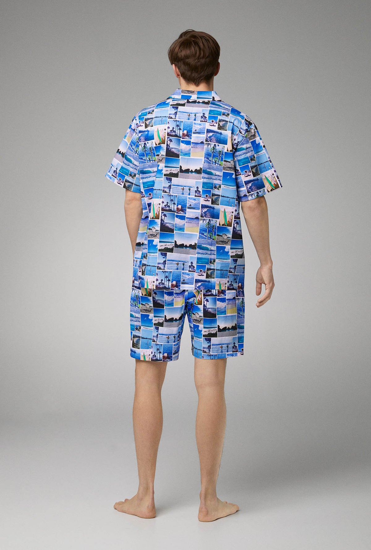 A man wearing blue short sleeve notch woven cotton poplin boxer pj set with beach day print.