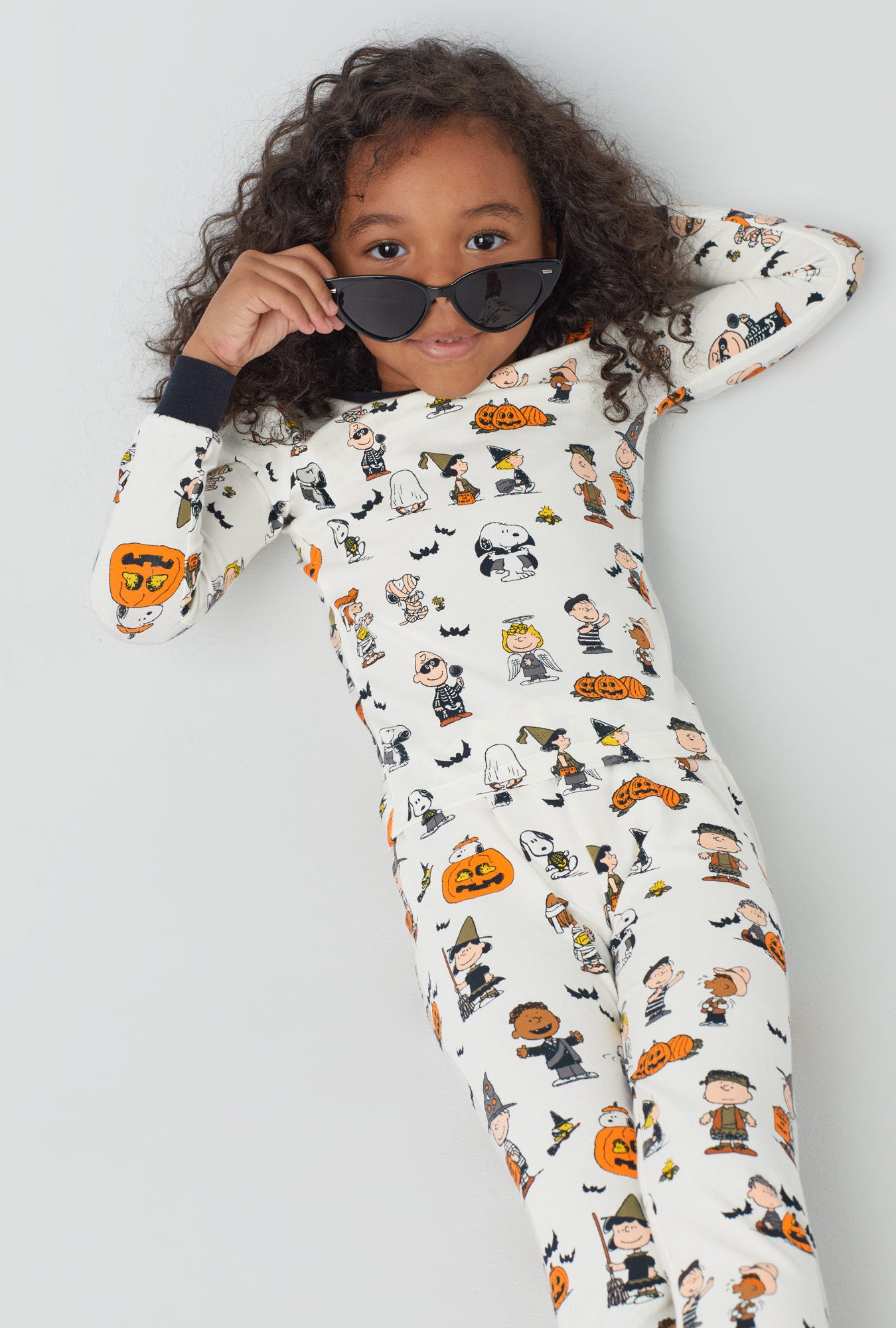 A girl wearing white long sleeve stretch jersey kids pj set with snoopys halloween print.