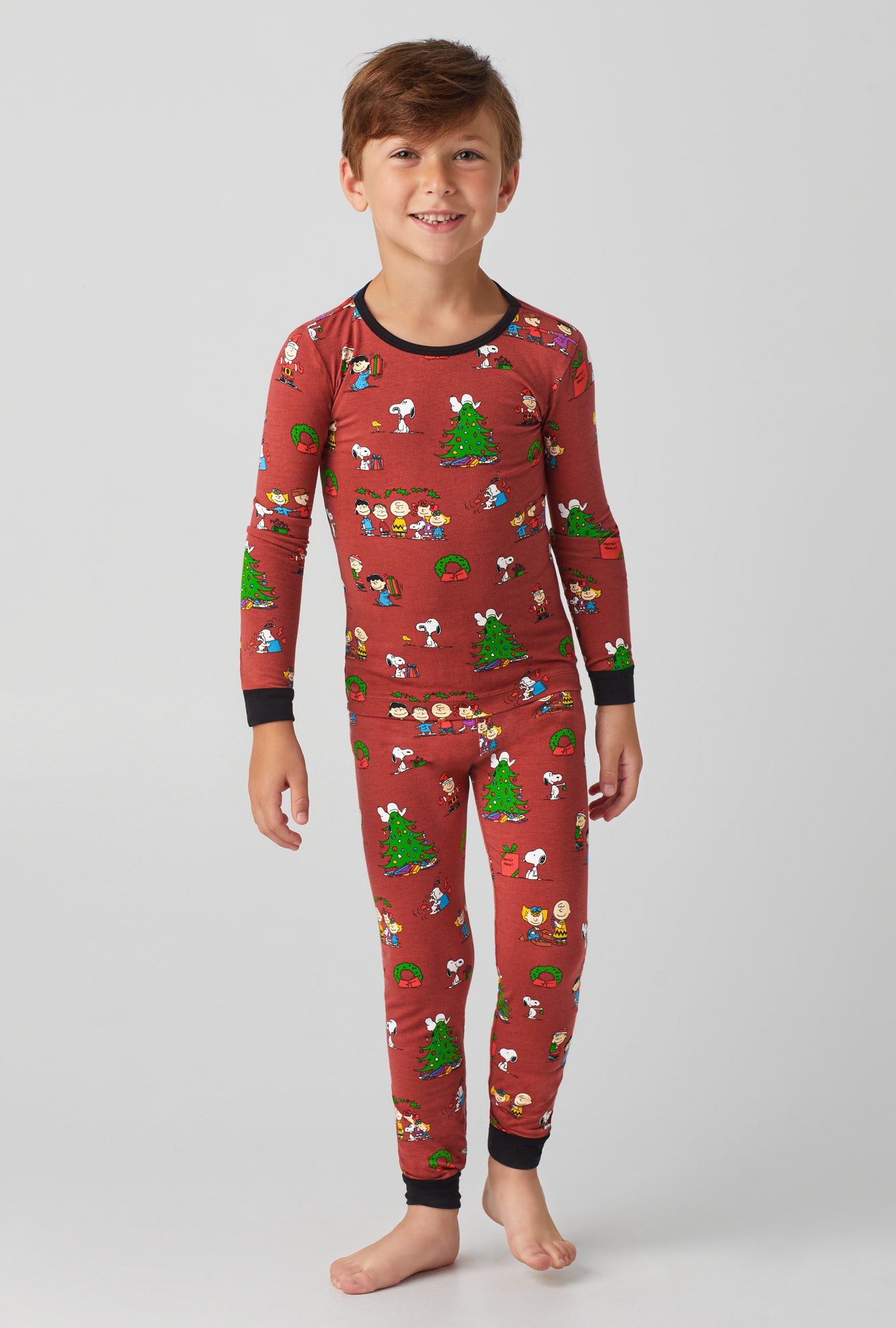 A boy wearing brown long sleeve stretch jersey kids pj set with bedhead x peanuts holiday party print.