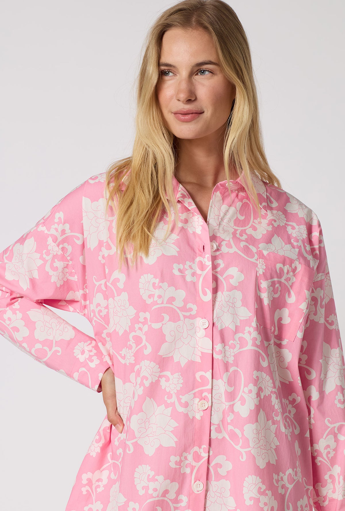 A Lady Wearing Dynasty Pink High Low Woven Cotton Poplin Boyfriend Shirt in a close up view pose