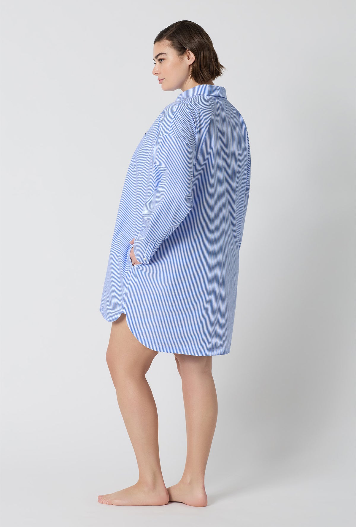 A Lady Wearing Plus Size French Stripe High Low Woven Supersoft Cotton Poplin Boyfriend Shirt in a side pose with one hand placed at the pocket