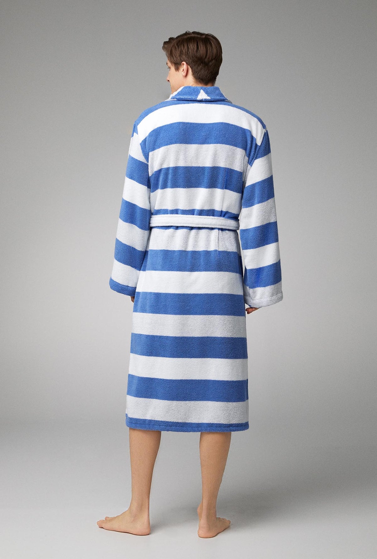 A man wearing white and blue unisex woven cotton loop turkish terry jacquard long robe with seaside stripe print.