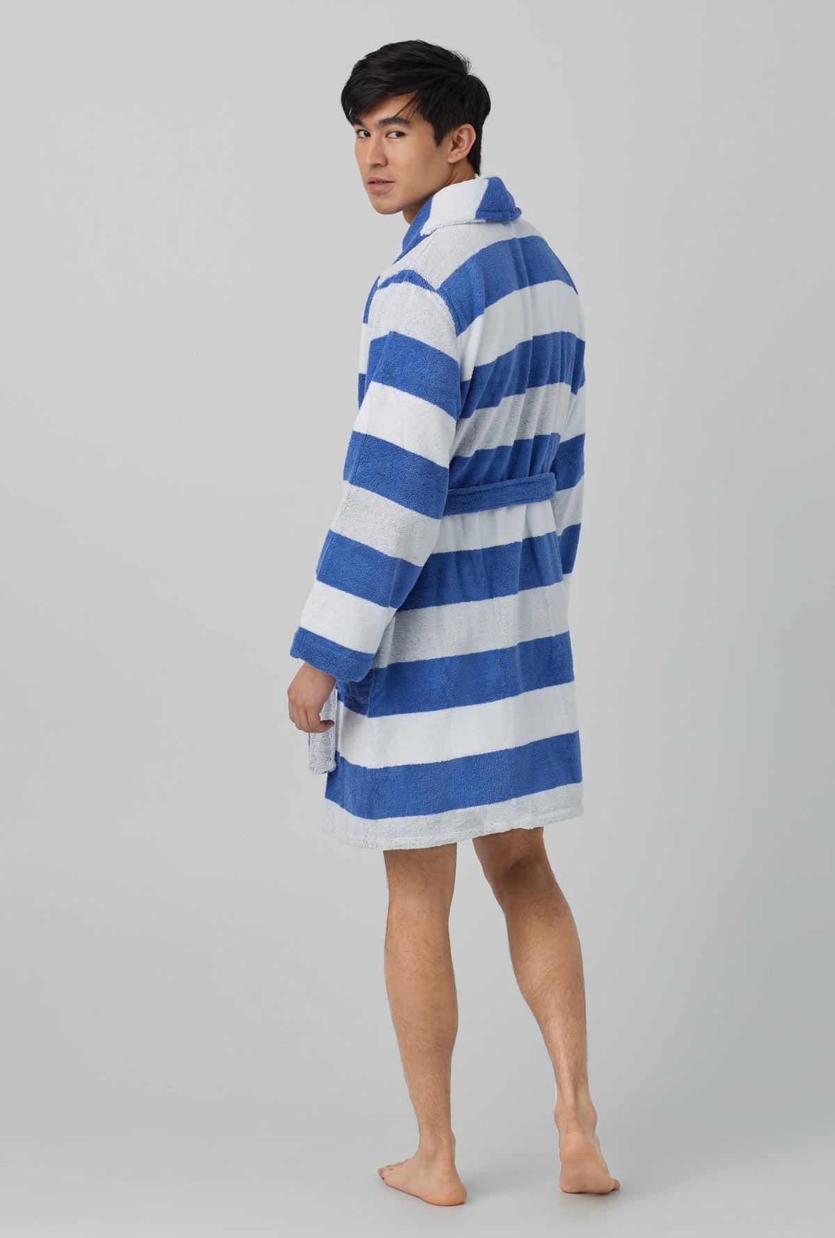 A man wearing white and blue unisex woven cotton loop turkish terrry jacquard short robe with seaside stripe print.