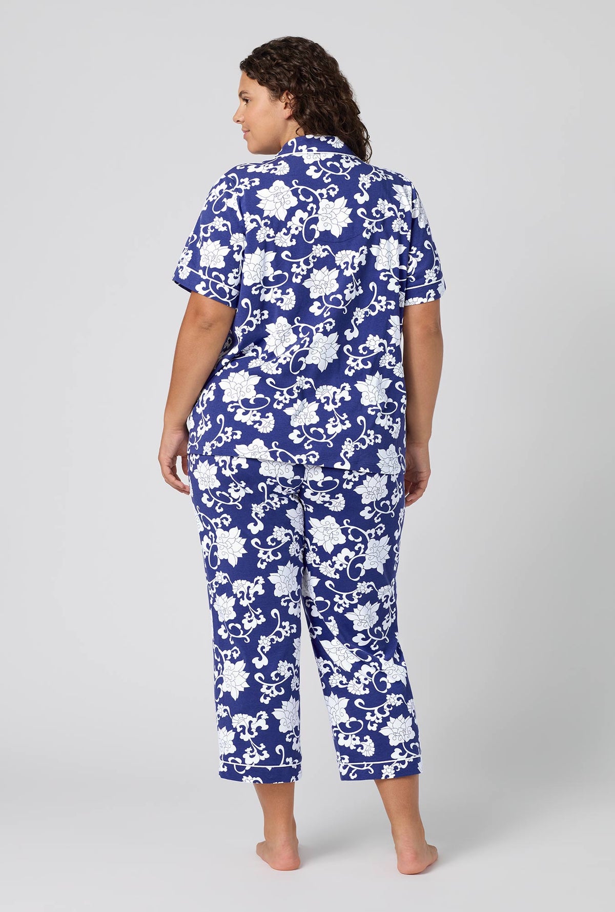 A Lady Wearing Plus Size Dynasty Blue Short Sleeve Classic Stretch Jersey Cropped Pj Set in a back view pose