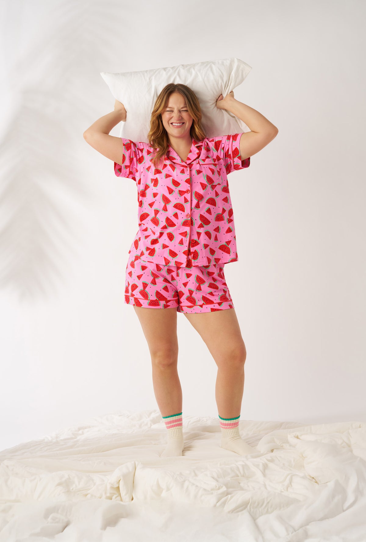 A lady wearing plus size Watermelon Crush Short Sleeve Classic Shorty Stretch Jersey Pj Set smiling while grabbing a pillow 