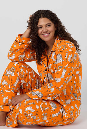 A Lady Wearing Plus Size Orange Spooky In The City Long Sleeve Classic Stretch Jersey Pj Set in a close up sitting pose