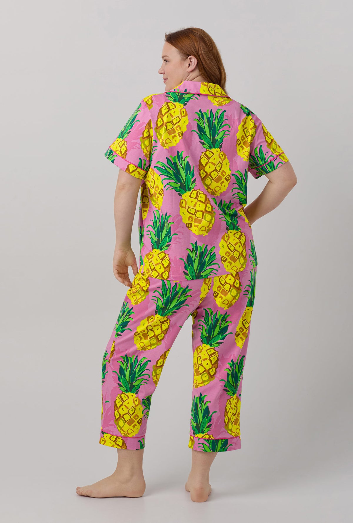 A lady wearing pink short sleeve classic stretch jersey cropped plus size pj set with trina turk pineapples print.