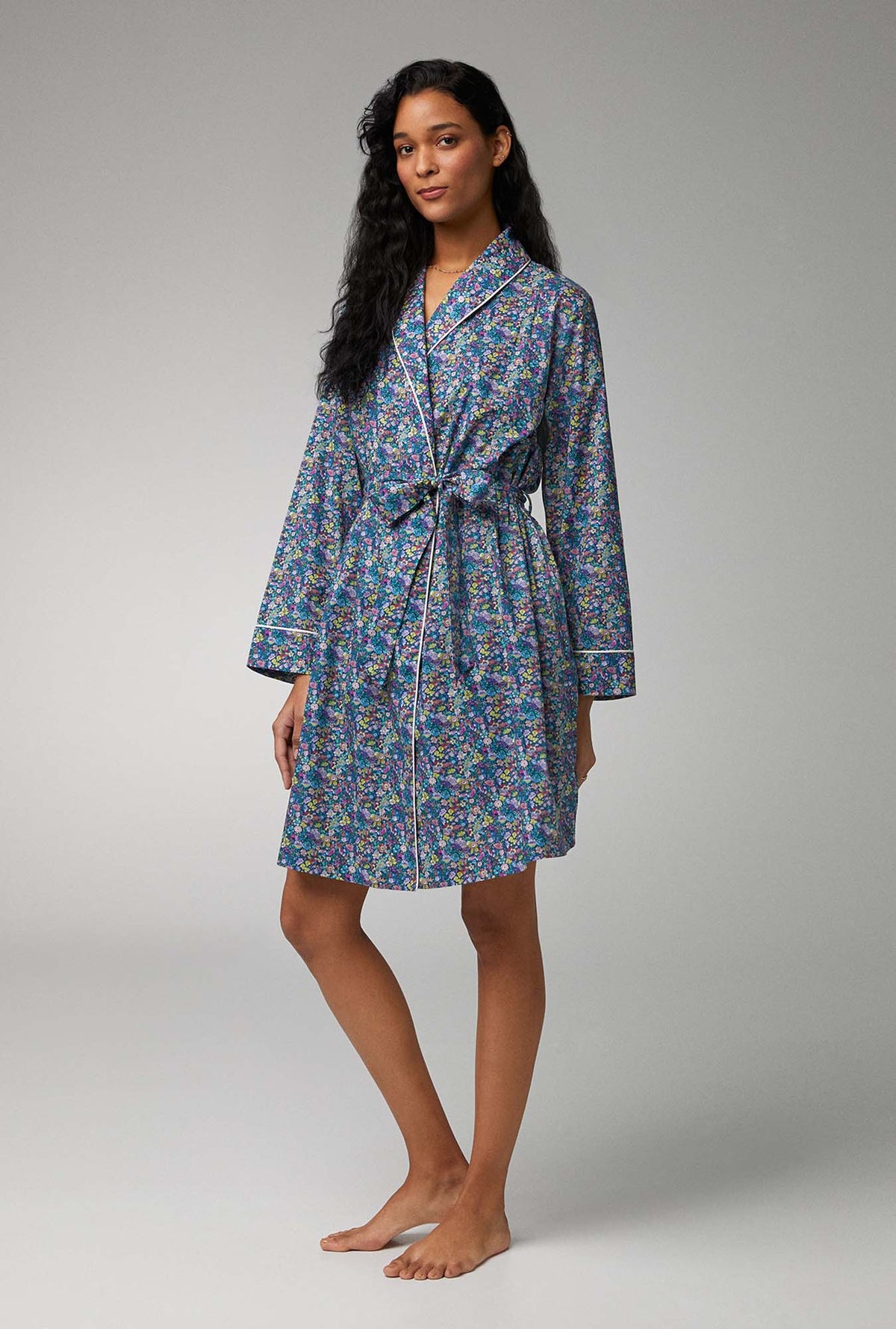 A lady wearing blue long sleeve shawl collar classic woven tana lawn robe made with liberty fabrics with classic garden print.