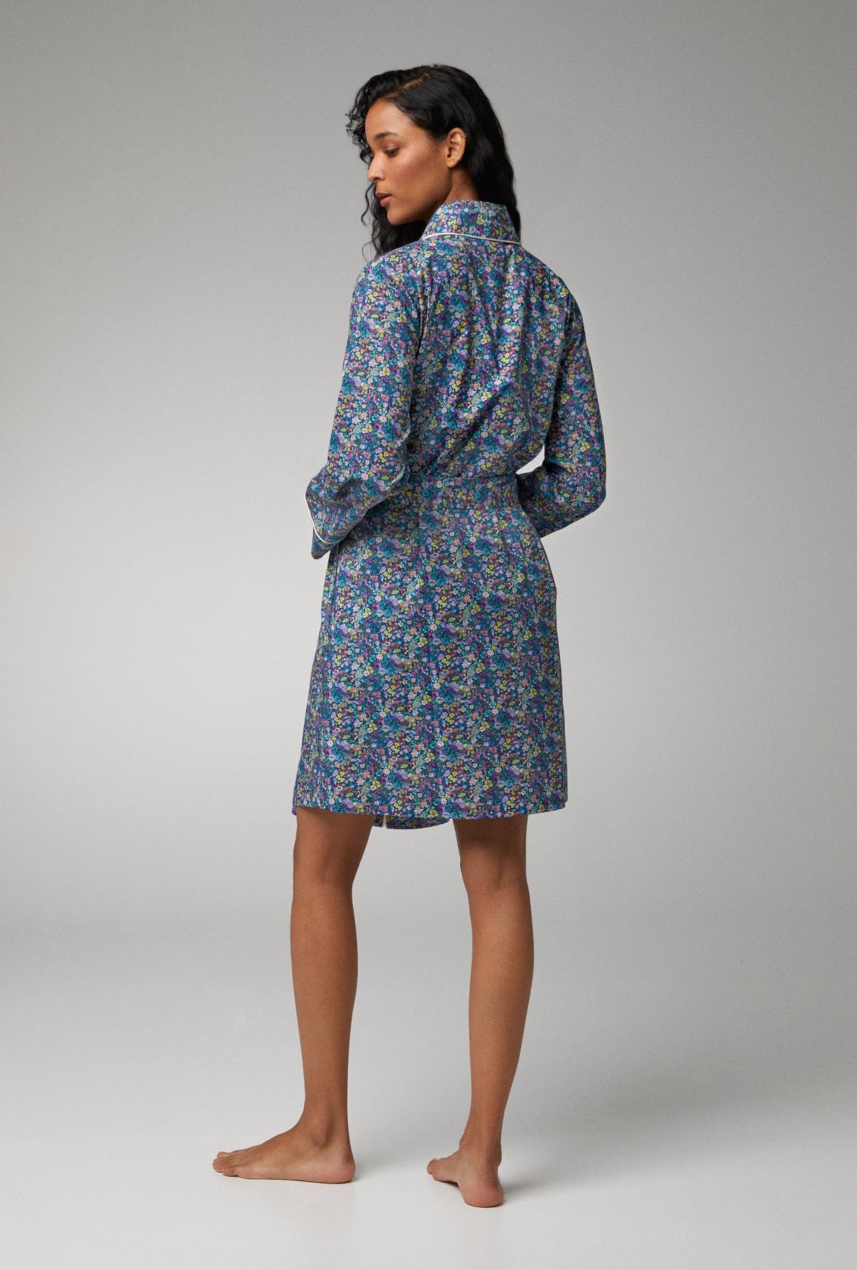 A lady wearing blue long sleeve shawl collar classic woven tana lawn robe made with liberty fabrics with classic garden print.