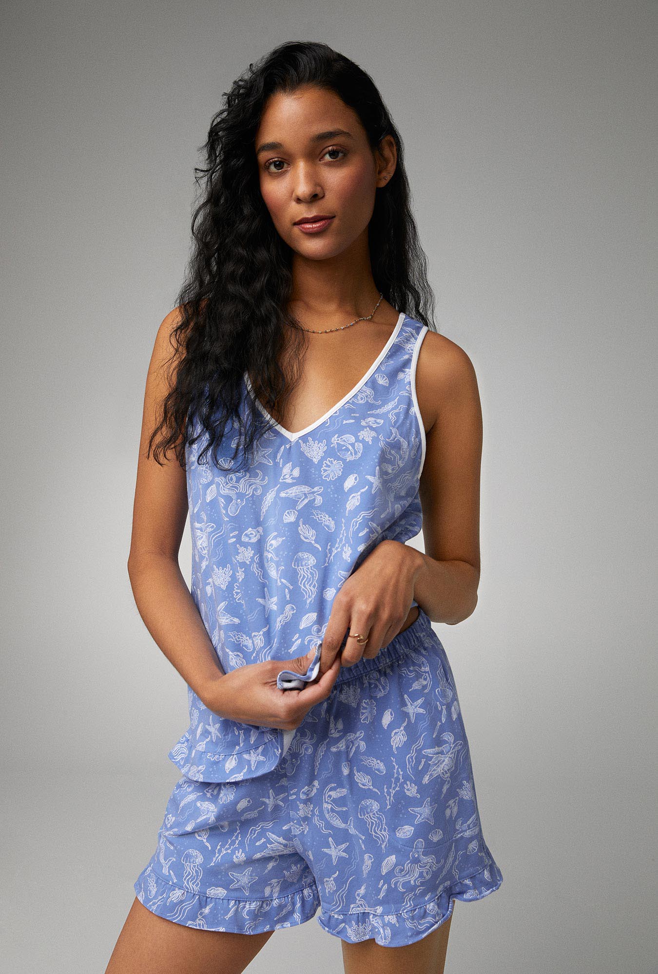 A lady wearing blue ruffle tank shorty stretch jersey pj set with high tide print.