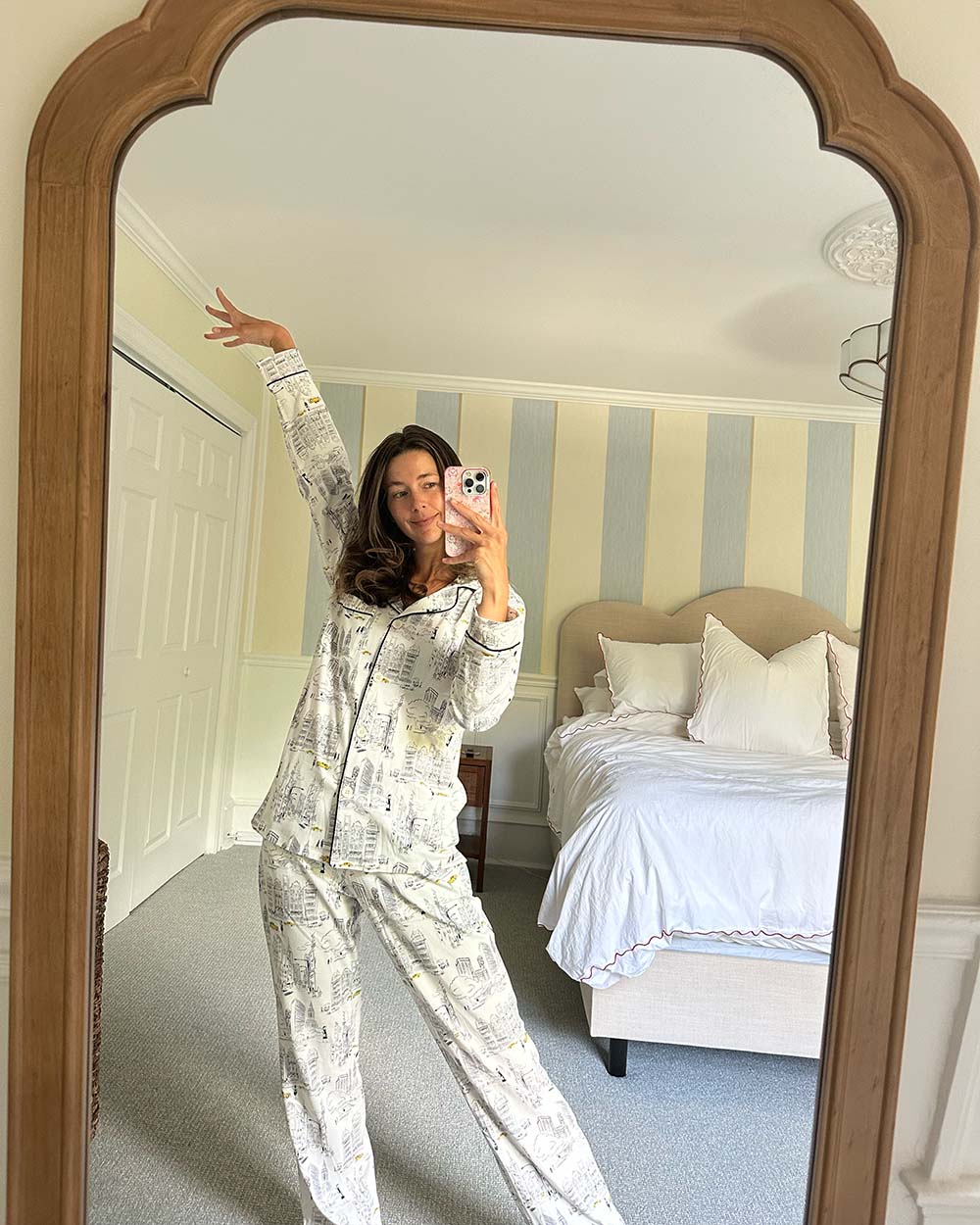 Person taking a mirror selfie wearing pajamas in a bedroom with striped walls.
