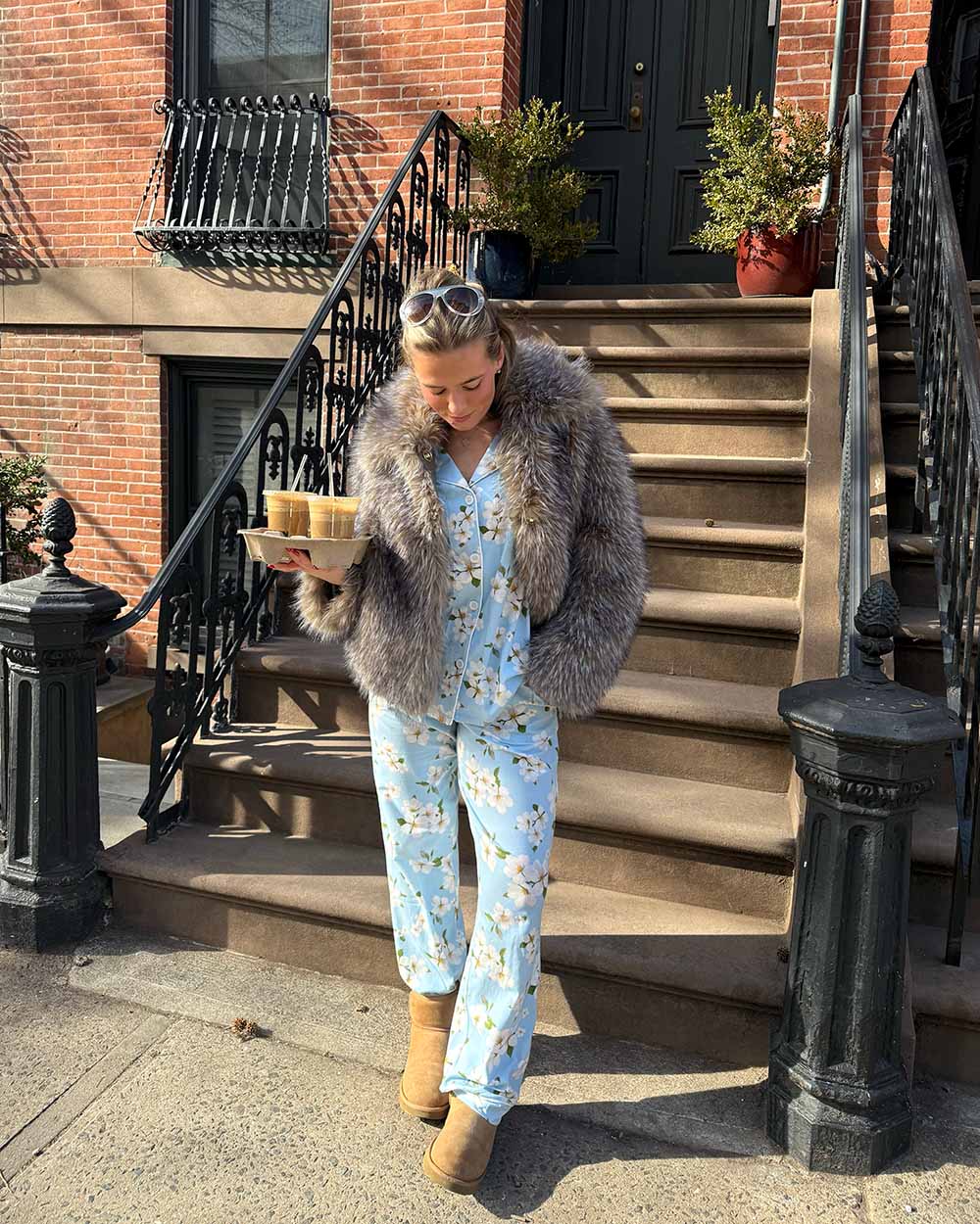 Person wearing a floral jumpsuit and fur coat on a city street.
