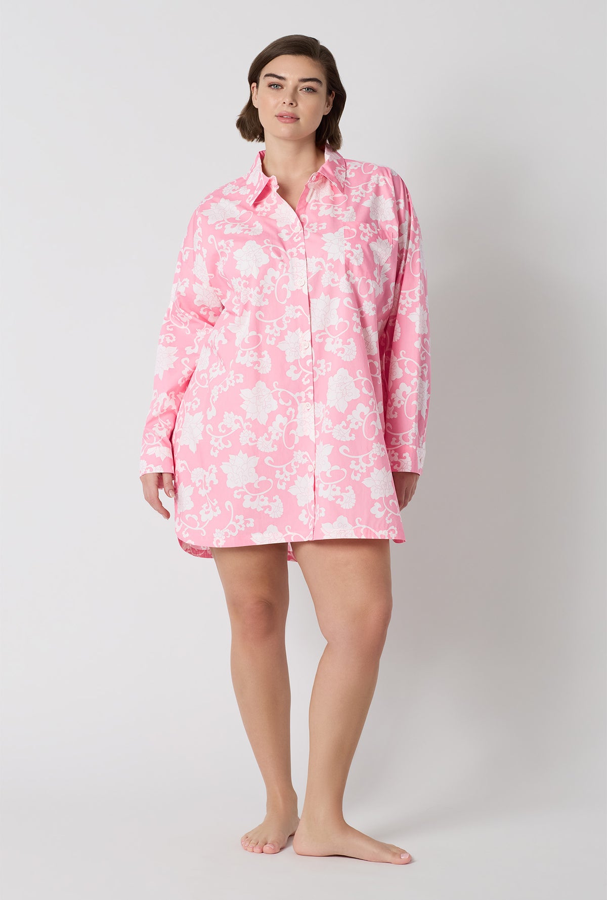 A Lady Wearing Plus Size Dynasty Pink High Low Woven Cotton Poplin Boyfriend Shirt in a standing pose