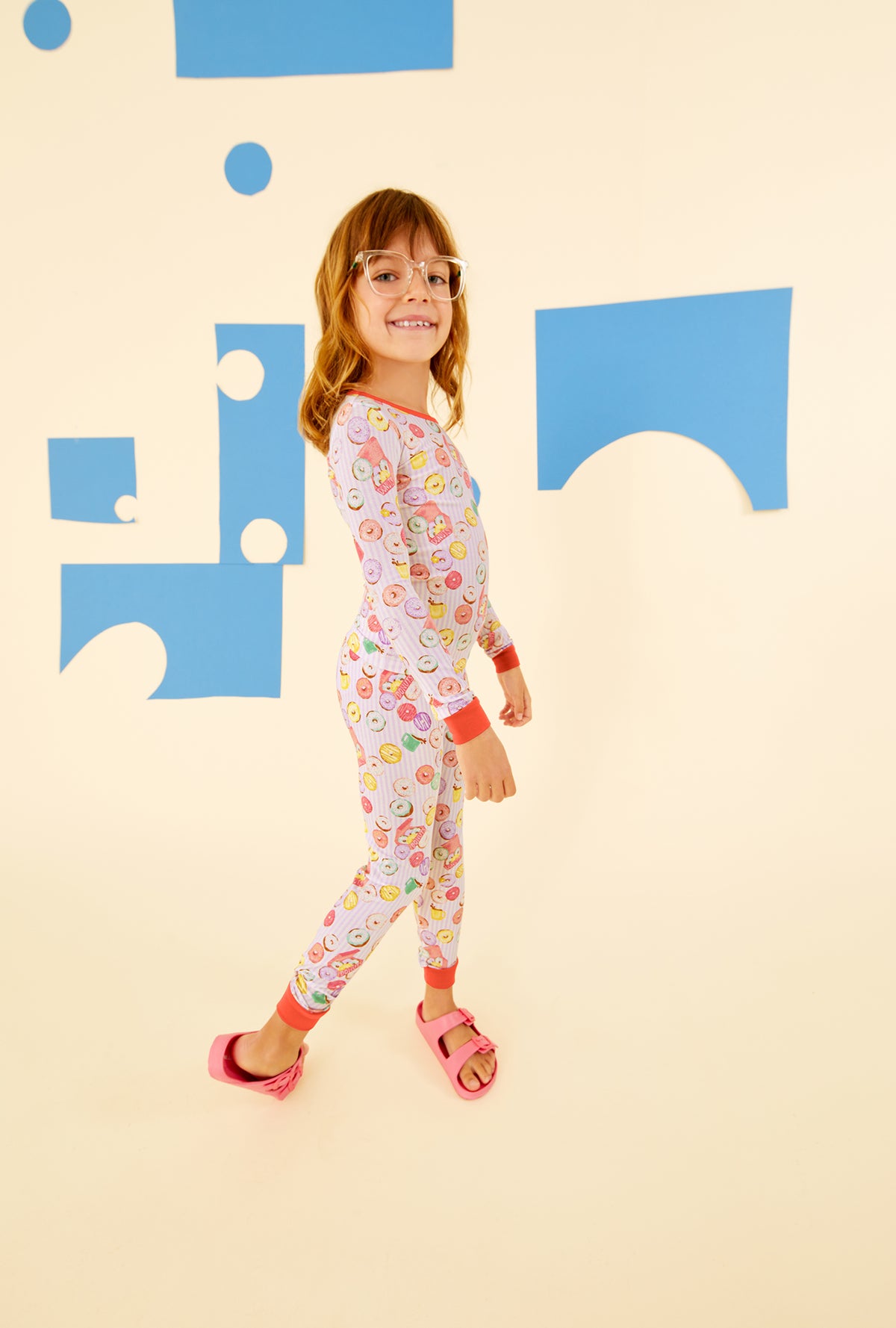  A kid wearing a purple long sleeve pajama set with donuts pattern.
