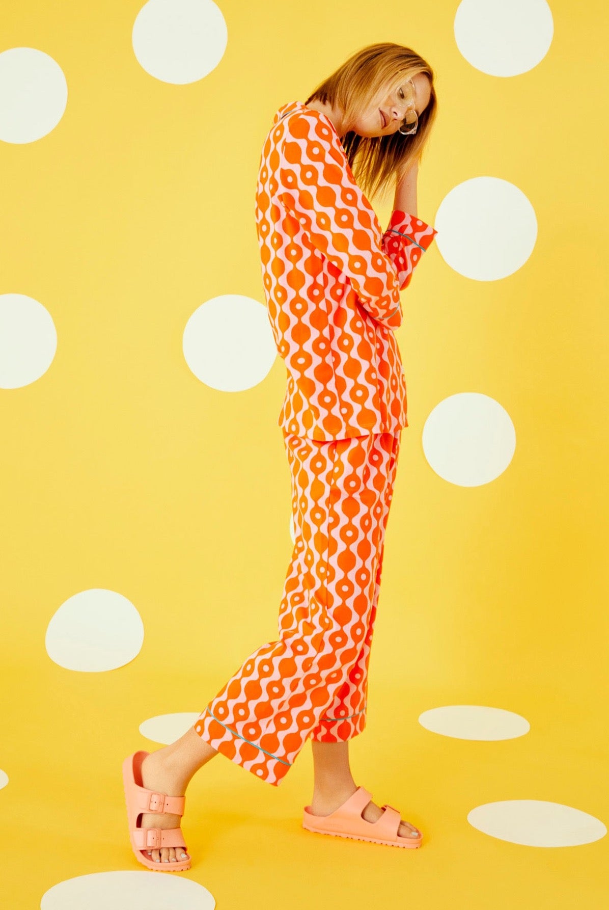 A lady wearing a orange quarter sleeve cropped pajama set with geometric pattern.
