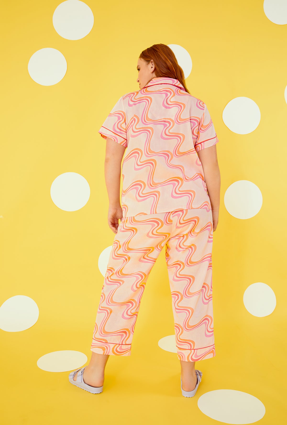 A lady wearing a orange pink short sleeve cropped pajama set plus with swirl pattern.
