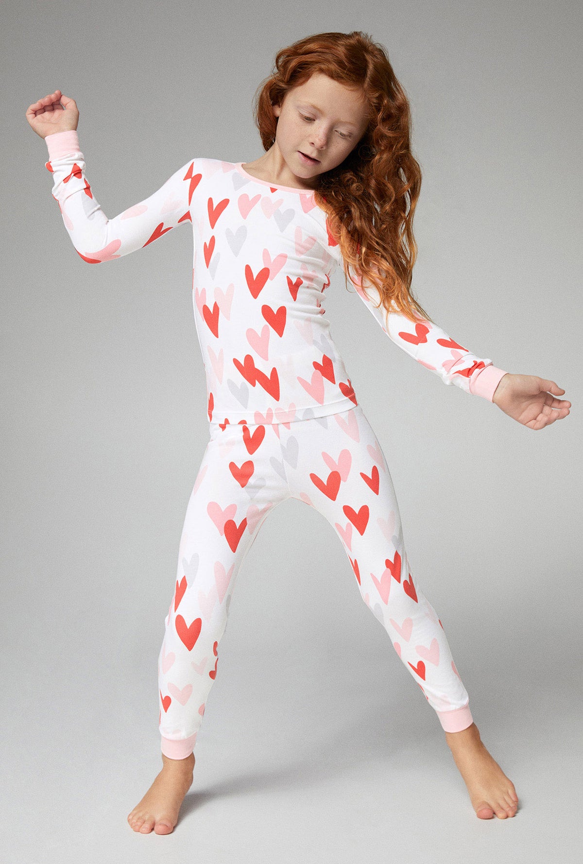 A girl wearing white long sleeve stretch jersey pj set with pink and red hearts print