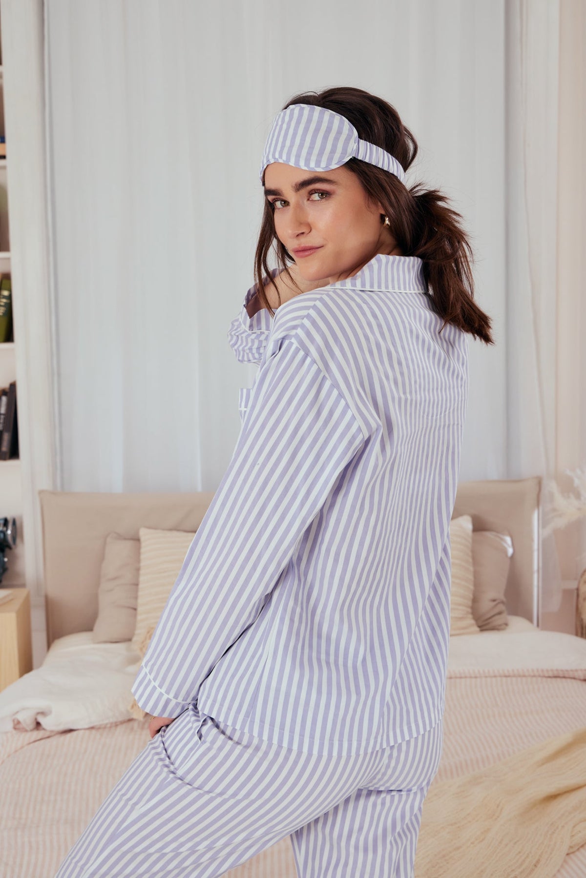 A lady wearing a long sleeve cotton sateen pj set with blue and white stripe pattern.