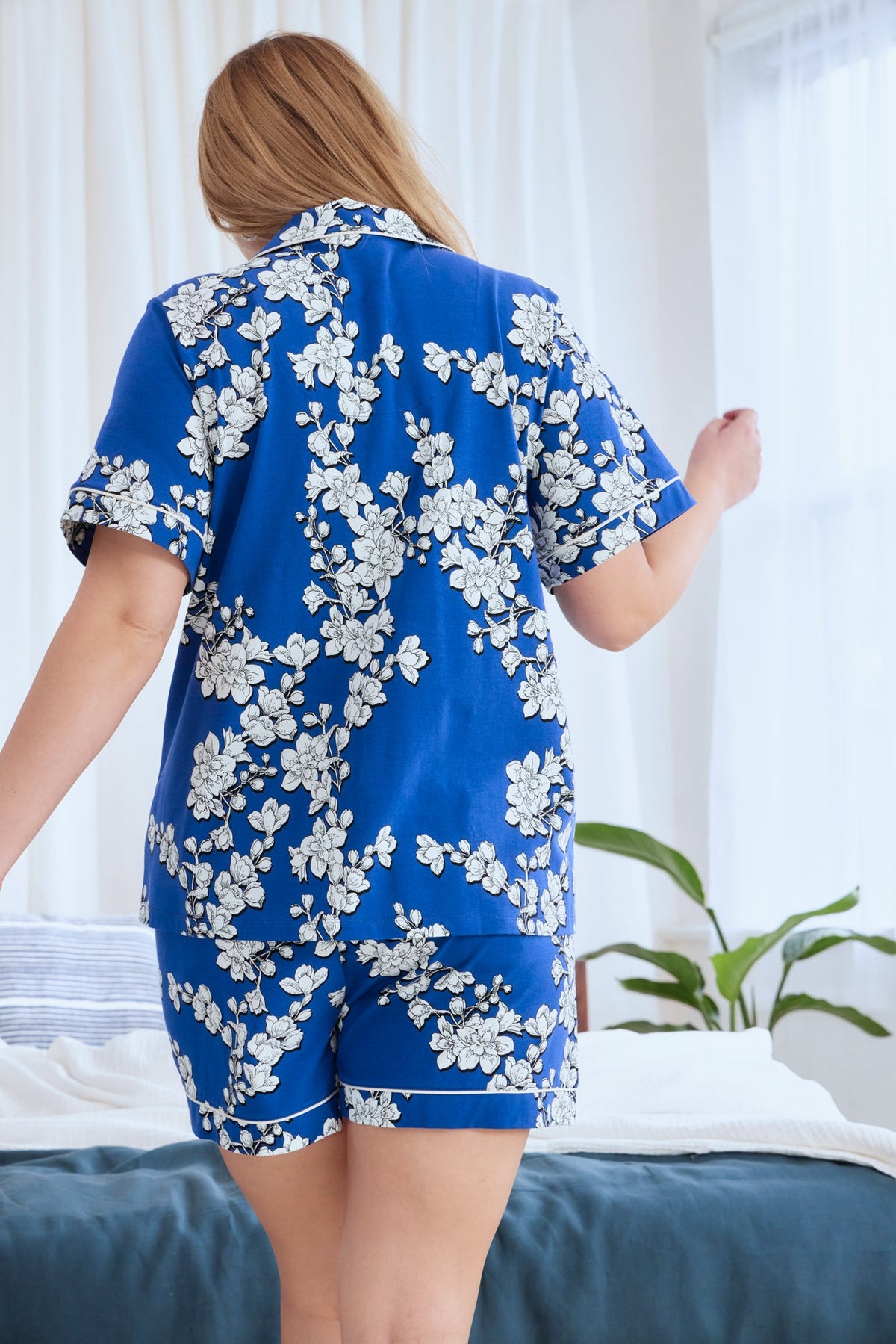 A lady wearing a blue short sleeve shorty plus size pj set with white blossom pattern.